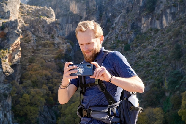 彼の後ろに岩の崖がある美しい景色の写真を撮る白人男性旅行者