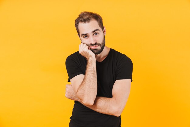 caucasian man in basic black t-shirt propping up his head in boredom isolated over yellow wall