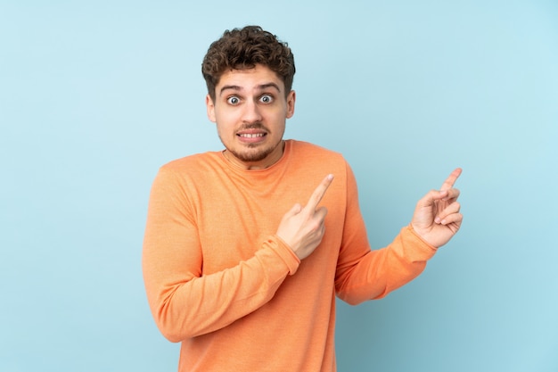 Caucasian man on blue wall frightened and pointing to the side
