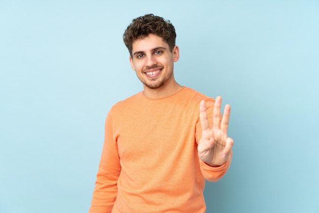 Uomo caucasico sulla parete blu felice e contando tre con le dita