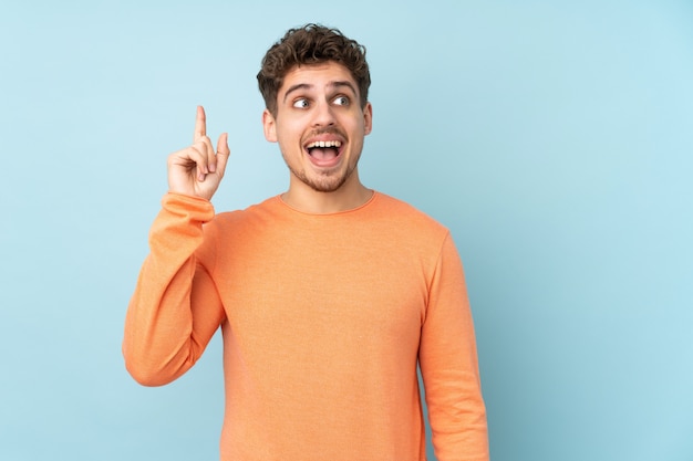 Caucasian man on blue wall intending to realizes the solution while lifting a finger up