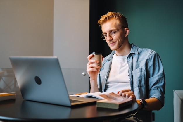 Caucasian man college student drinking coffee and studying with laptop distantly