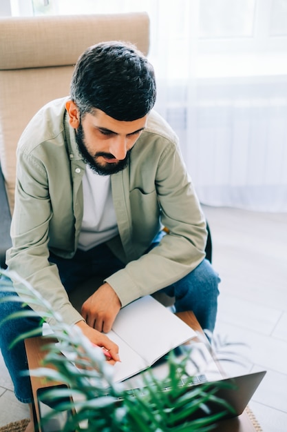 Caucasian man college student, studying with laptop distantly preparing for test exam writing essay doing homework at home, distantly education concept.