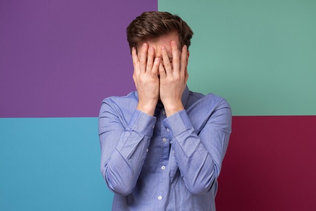 Caucasian man covering his face feeling humiliated studio shot