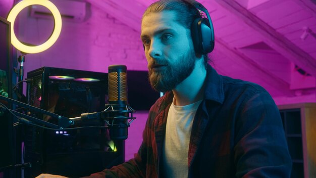 caucasian man cyber sport streamer gamer influencer in headphones talking microphone mic radio vlog addicted guy streaming at home neon male blogger typing play computer online games communicate blog