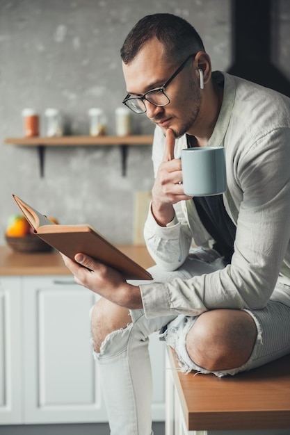 趣味のビジネスマンを読んでキッチンで本を読みながらコーヒーを飲む白人男性