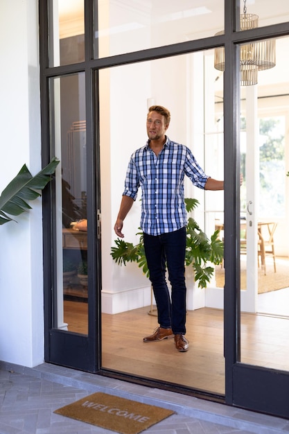 Caucasian man enjoying his time at home, standing at his open front door, greeting a visitor, looking away from the camera and smiling