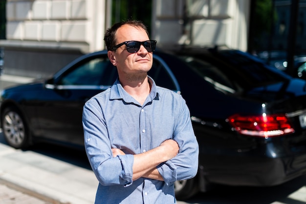 Caucasian man forty years old businessman in the city in the summer on the background of the car.