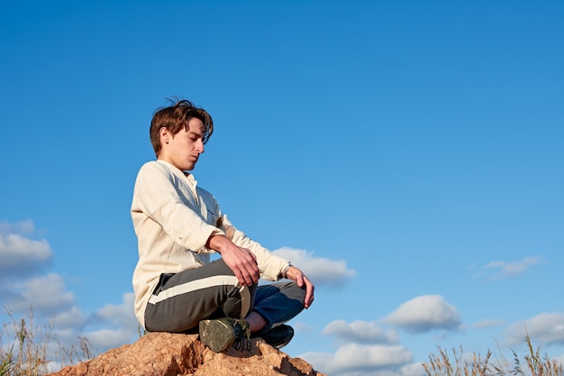Кавказский мужчина из Испании в бежевой рубашке медитирует сидя на фоне облачного неба