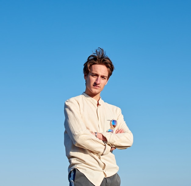 A Caucasian man from Spain in a beige shirt with glasses hanging off of him on clear sky