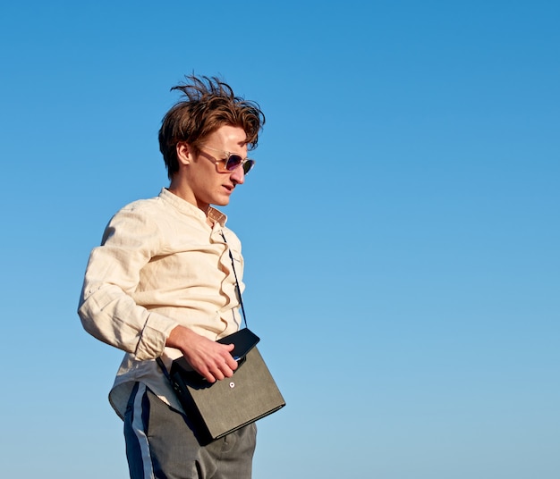 A Caucasian man from Spain standing and closing his black handbag on clear sky background