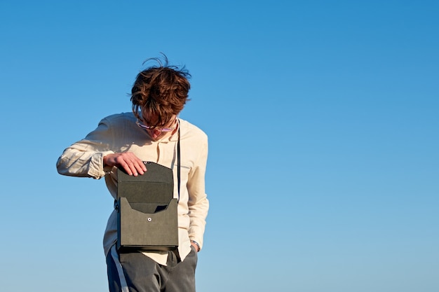 A Caucasian man from Spain standing and opening his black handbag on clear sky background