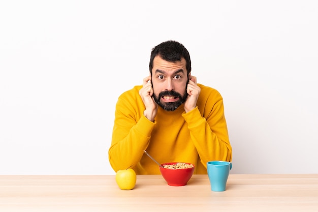 Caucasian man having breakfast in a table frustrated and covering ears