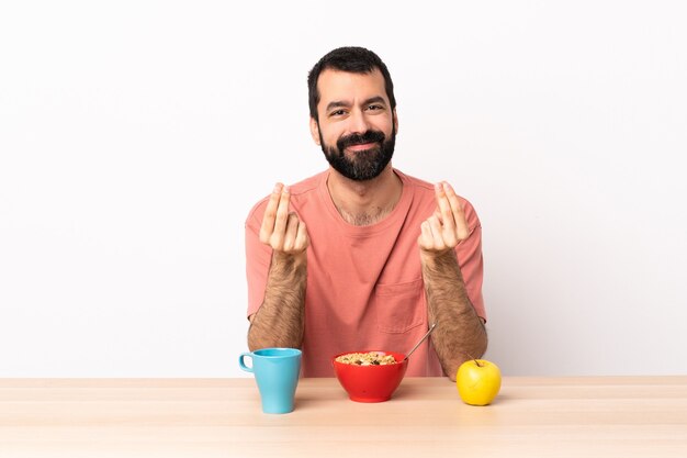 Uomo caucasico che mangia prima colazione in una tabella che fa gesto di soldi.