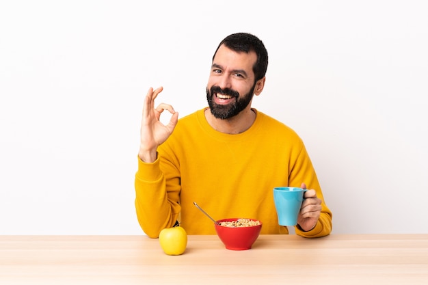 Кавказский мужчина завтракает в столе, показывая пальцами знак ОК