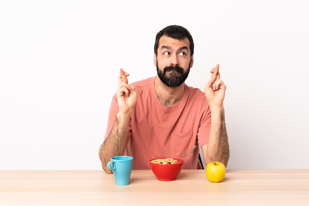 Caucasian man having breakfast in a table with fingers crossing and wishing the best