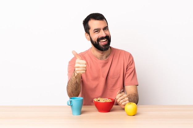 Кавказский мужчина завтракает за столом с большими пальцами руки вверх