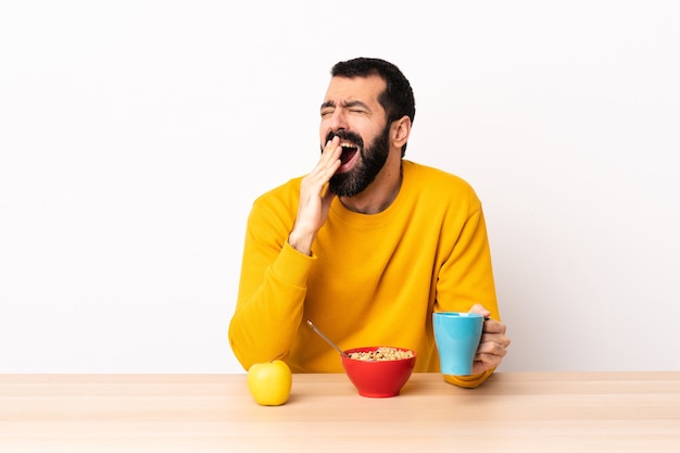 Caucasian man having breakfast in a table yawning and covering wide open mouth with hand