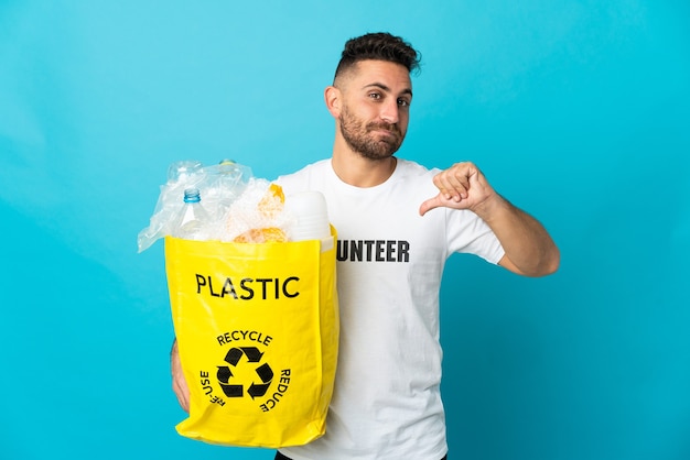 Caucasian man holding a bag full of plastic bottles to recycle isolated on blue background proud and self-satisfied