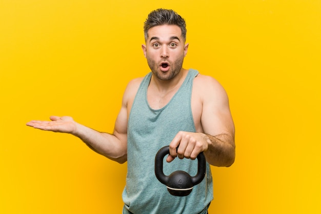 Caucasian man holding a bumbbell impressed holding copy space on palm.