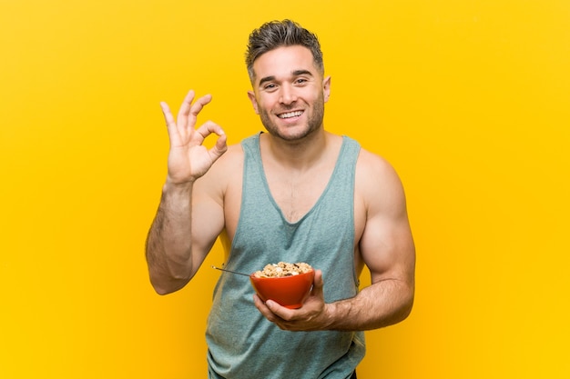 Caucasian man holding a cereal bowl cheerful and confident showing ok gesture.