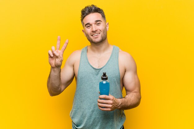 Caucasian man holding an energy drink showing number two with fingers.