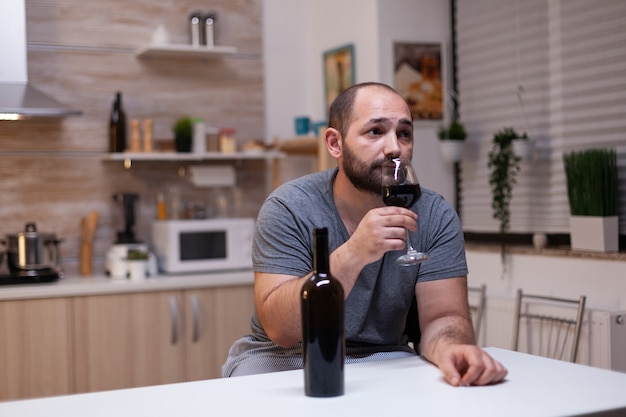 Caucasian man holding glass of wine sitting in kitchen