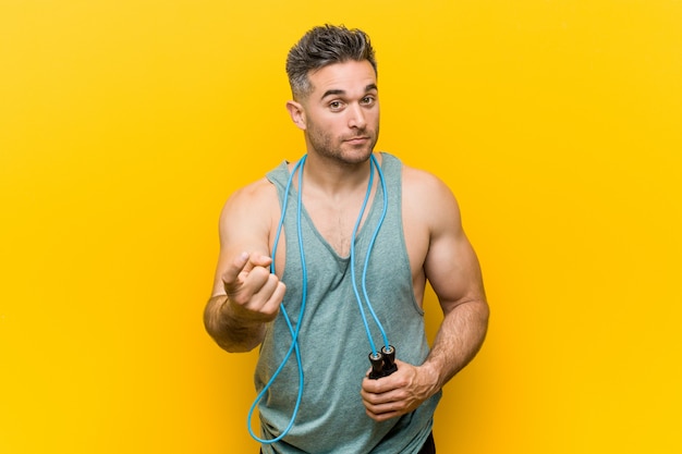 Caucasian man holding a jump rope pointing with finger at you as if inviting come closer.