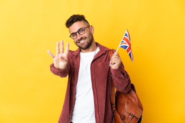 幸せな黄色の背景に分離されたイギリスの旗を保持し、指で4を数える白人男性