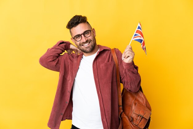 Caucasian man holding an United Kingdom flag isolated on yellow background laughing