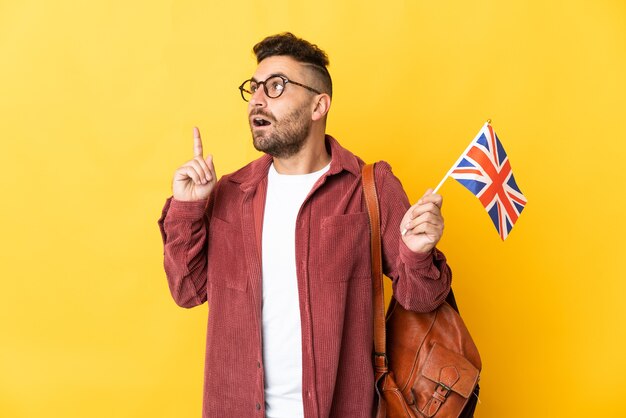 Caucasian man holding an United Kingdom flag isolated on yellow background thinking an idea pointing the finger up