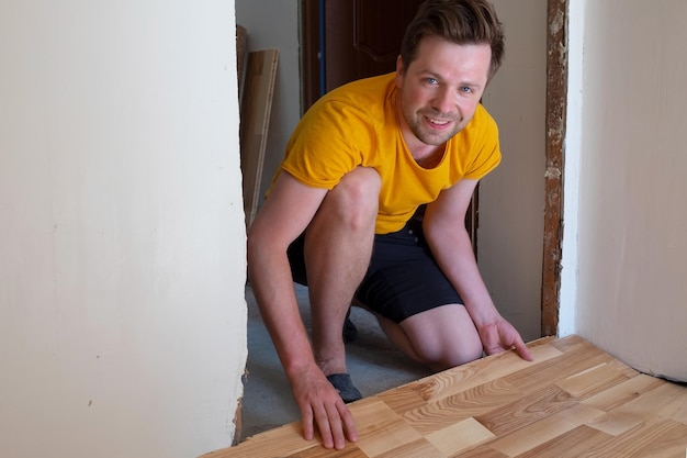 Uomo caucasico che installa il parquet in legno durante i lavori di pavimentazione