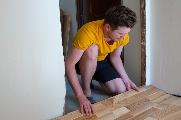 Caucasian man installing wood parquet board during flooring work