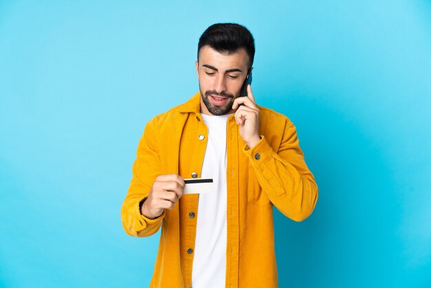 Caucasian man over isolated blue background buying with the mobile with a credit card