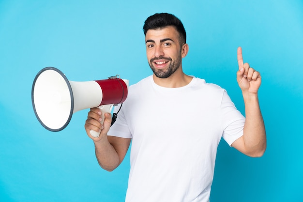 Caucasian man over isolated blue wall holding a megaphone and pointing up a great idea