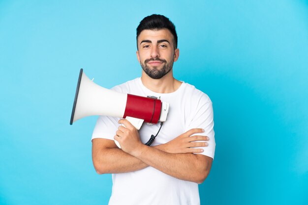 Caucasian man over isolated blue wall holding a megaphone and smiling