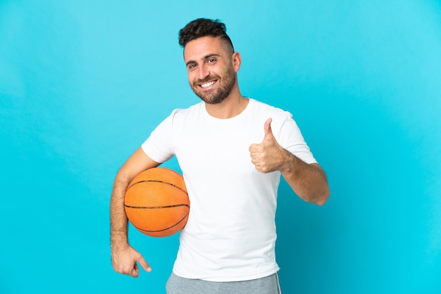 Кавказский мужчина изолирован на синей стене, играет в баскетбол и с большим пальцем вверх
