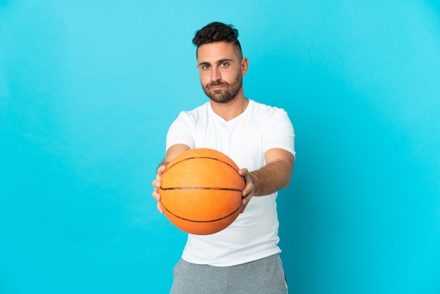 Caucasian man isolated on blue wall playing basketball