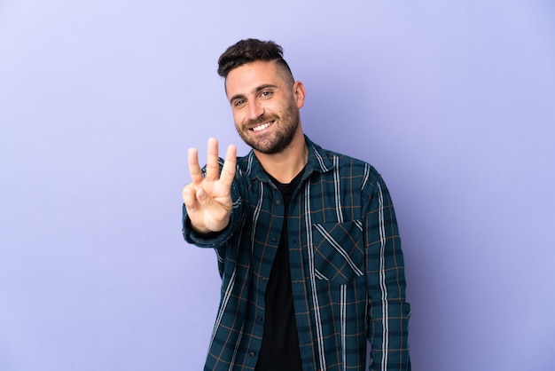 Caucasian man isolated on purple background happy and counting three with fingers