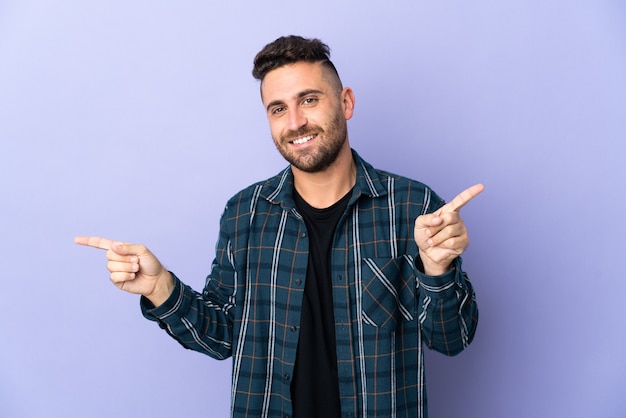 Caucasian man isolated on purple background pointing finger to the laterals and happy