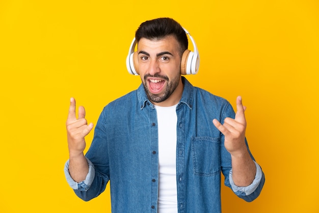 Caucasian man over isolated yellow listening music making rock gesture