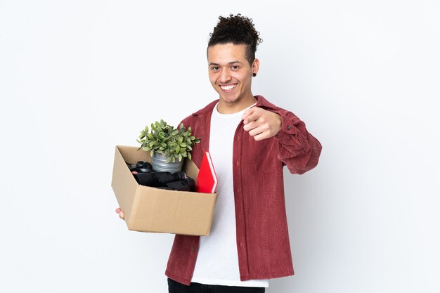 Caucasian man making a move while picking up a box full of things over isolated white background points finger at you with a confident expression