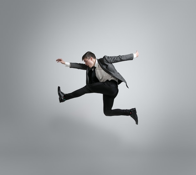 Caucasian man in office clothes running isolated on grey studio background