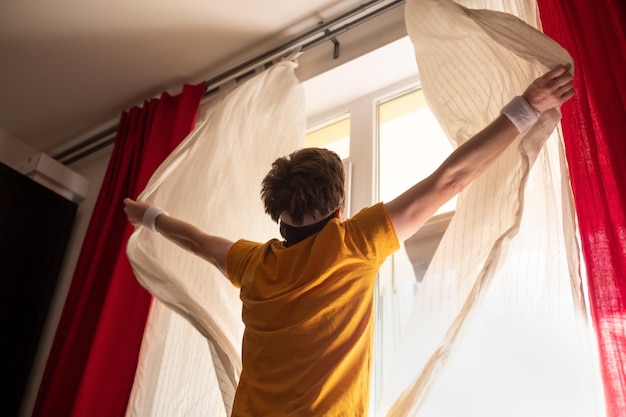 Foto uomo caucasico che apre le tende sulla finestra alla luce del mattino