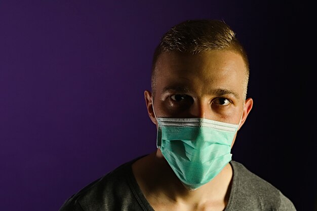 Caucasian man portrait in a medical gauze mask on dark blue background.