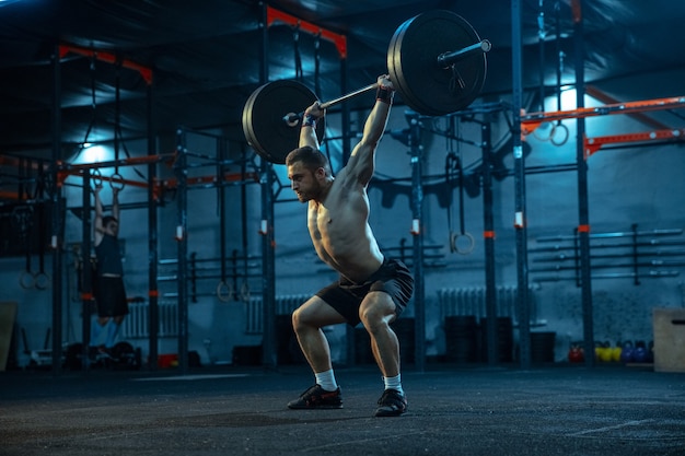 Foto uomo caucasico che pratica sollevamento pesi in palestra. modello sportivo maschile caucasico che si allena con bilanciere, sembra sicuro e forte. body building, stile di vita sano, movimento, attività, concetto di azione.