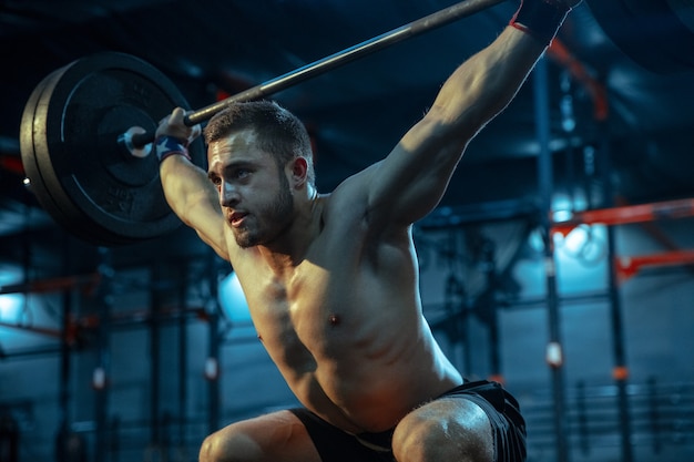 Caucasian man practicing in weightlifting in gym. Caucasian male sportive model training with barbell, looks confident and strong. Body building, healthy lifestyle, movement, activity, action concept.