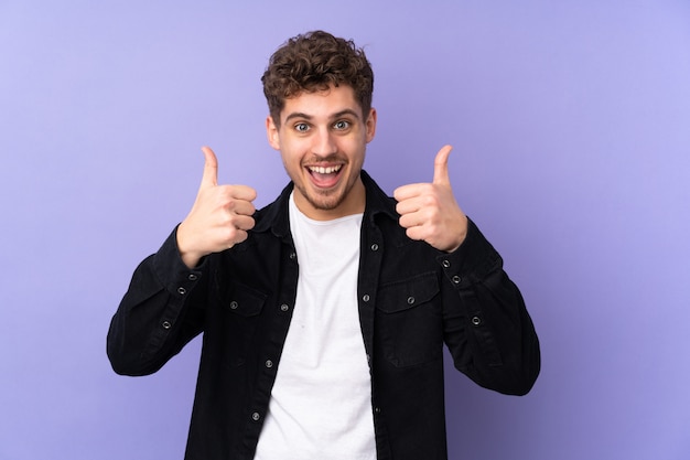 Caucasian man on purple wall giving a thumbs up gesture