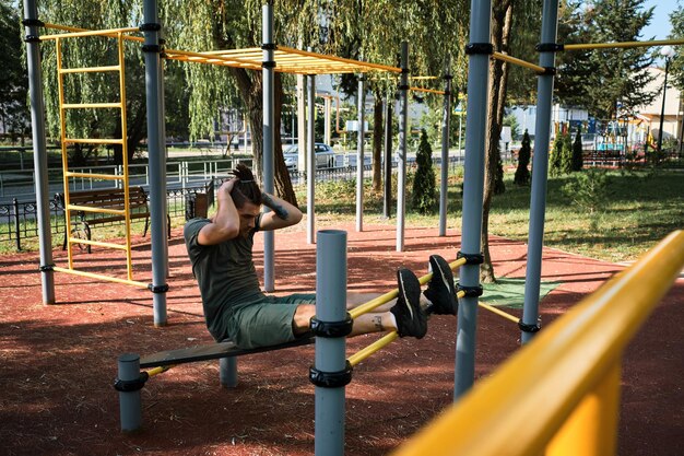 Caucasian man shakes his abs on street sports ground equipped with exercise equipment