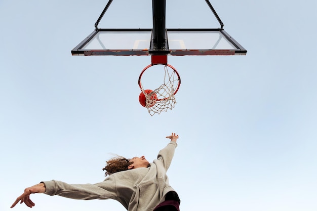 Caucasian man shooting in a basketball hoop seen from below with the sky in the background concept of urban sport outdoors copy space for text